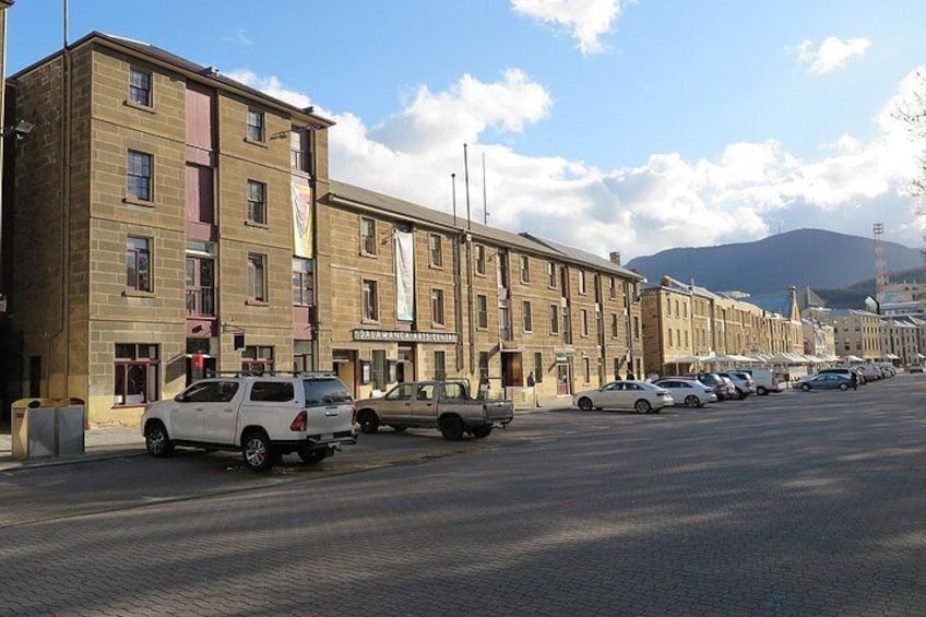A street lined with multi-story buildings, parked cars, and a mountainous background. 3