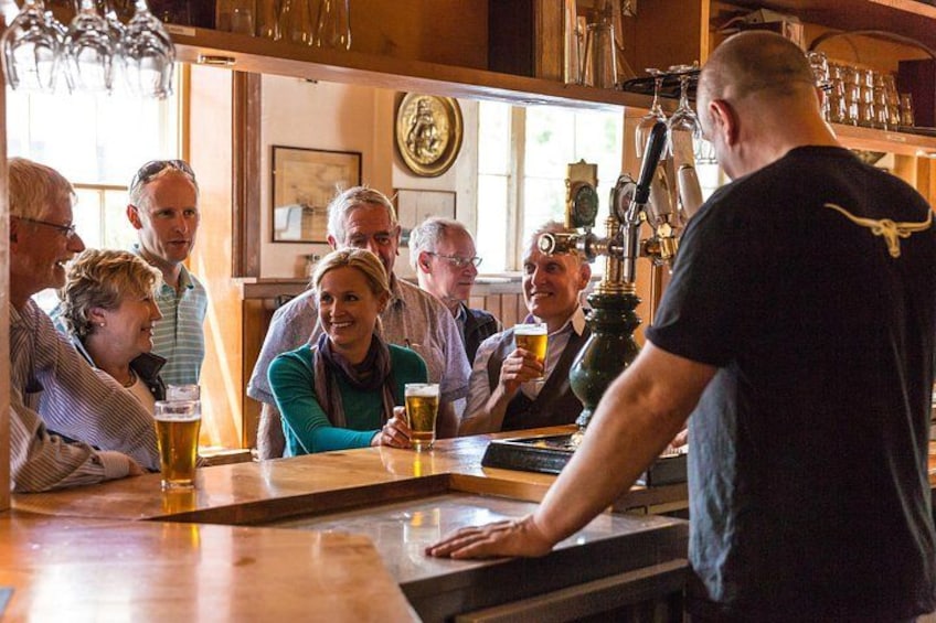A group of people at a bar with a bartender serving beer. 1