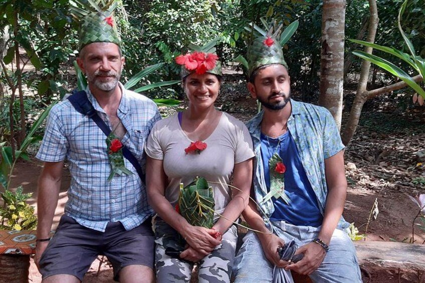Tre personer sidder udendørs, iført hatte med røde blomster. 4