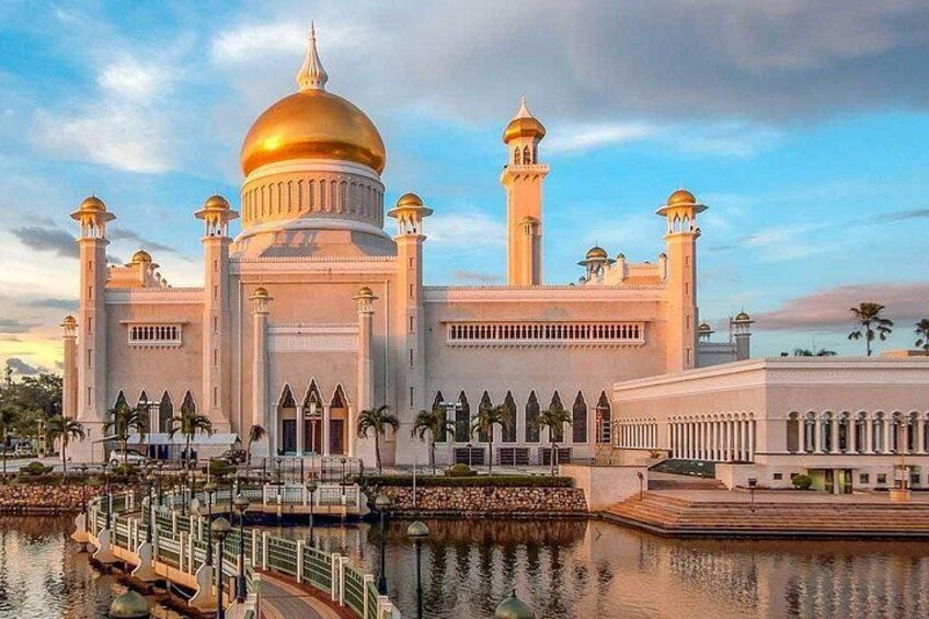 Een grote moskee met een gouden koepel en meerdere minaretten, omgeven door water en palmbomen. 2
