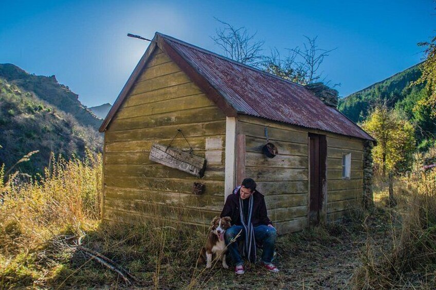 A wooden cabin with a metal roof, surrounded by tall grass and hills. 4