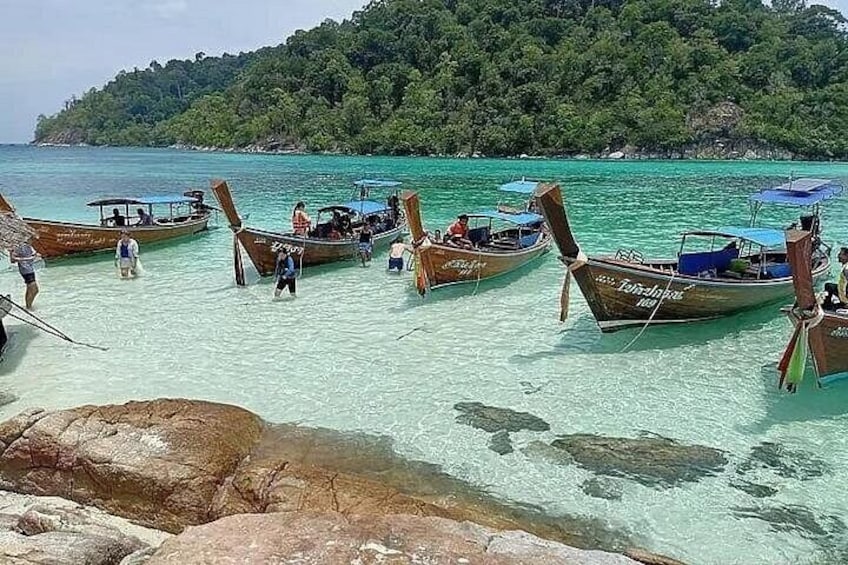Una playa con agua turquesa cristalina, varias embarcaciones de madera tradicionales y una colina cubierta de bosque al fondo. 2