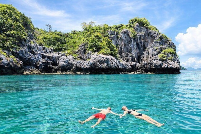 Dos personas flotando en un mar azul cristalino con una isla rocosa al fondo. 5