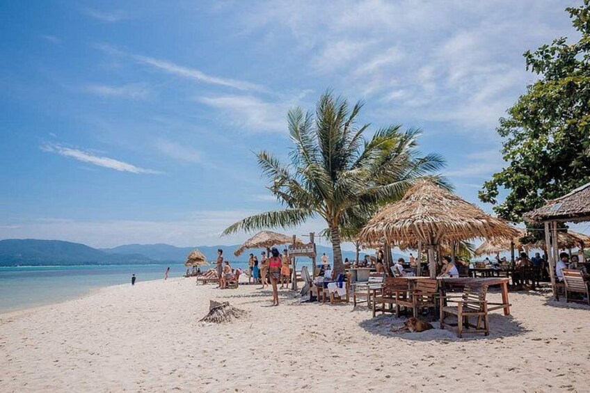 A beach with thatched umbrellas, wooden tables, and people relaxing. 3