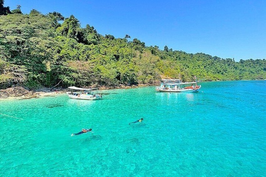 Un mar turquesa transparente con dos barcos y un nadador. 3