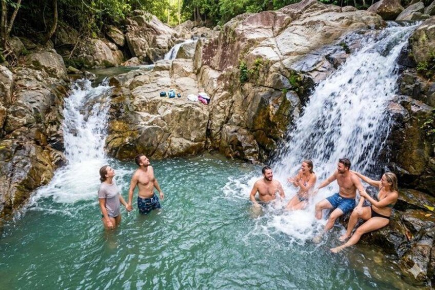A group of people enjoying a natural hot spring surrounded by rocky terrain and a waterfall. 2