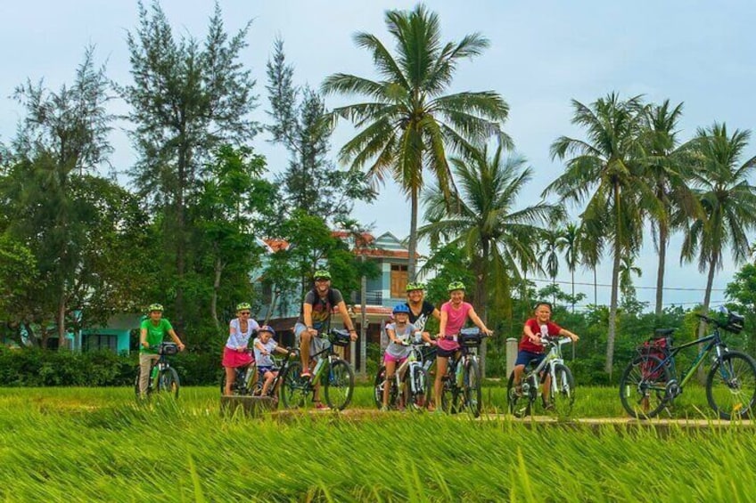 Een groep mensen fietst door een weelderig groen veld, met palmbomen op de achtergrond. 4