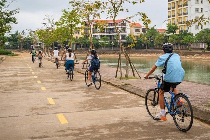 Un groupe de cyclistes sur une piste asphaltée, près d’une étendue d’eau, avec des bâtiments en arrière-plan. 3