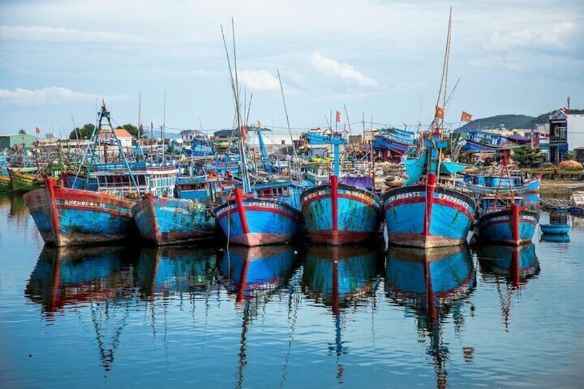 Verschillende kleurrijke vissersboten liggen afgemeerd in een haven, met een stad op de achtergrond. 2