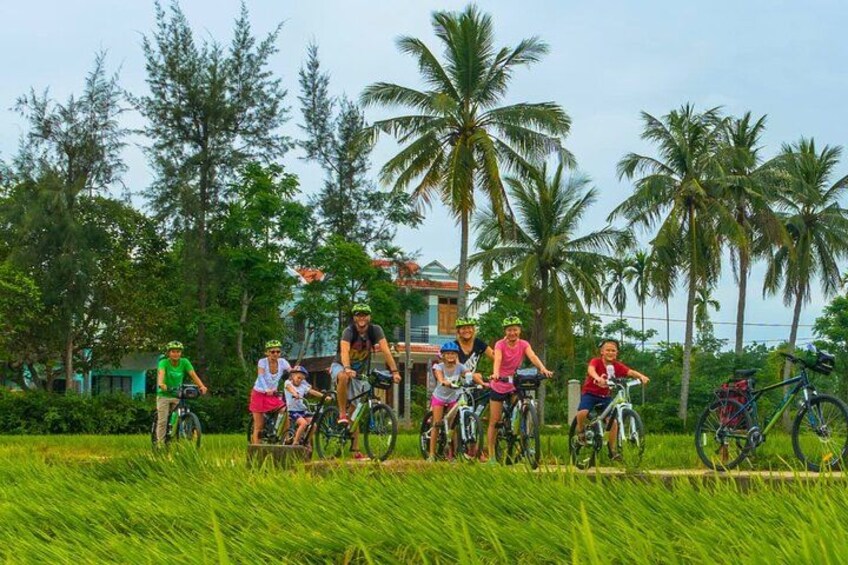 Een groep mensen die op fietsen rijden in een veld met palmbomen en een gebouw op de achtergrond. 4