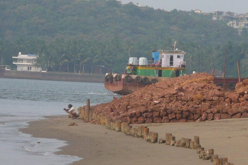 A boat on a beach, a pile of rocks, and a building in the background. 4
