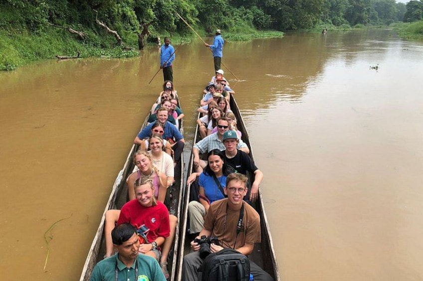 A group of people in a longboat on a river, surrounded by greenery. 1