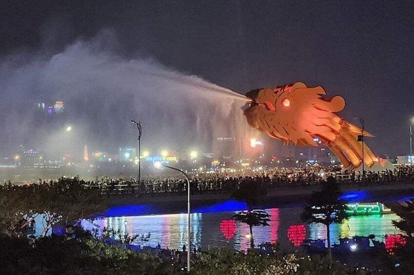 A large illuminated dragon sculpture spraying water, a crowd of people, and a cityscape with lights in the background. 2