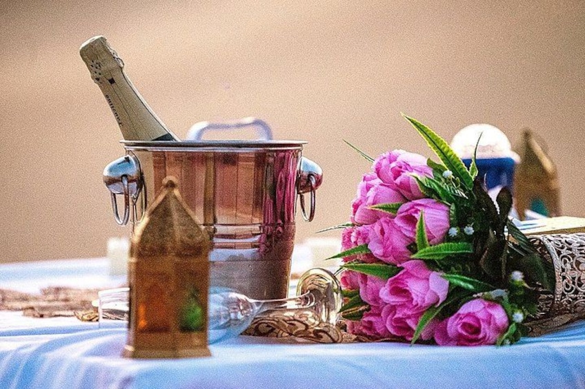En champagneflaske, et glas og en buket lyserøde blomster på et bord. 4