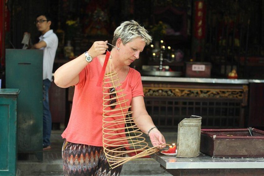 A person in a red shirt and patterned pants performing a ritual with a string of incense sticks. 5
