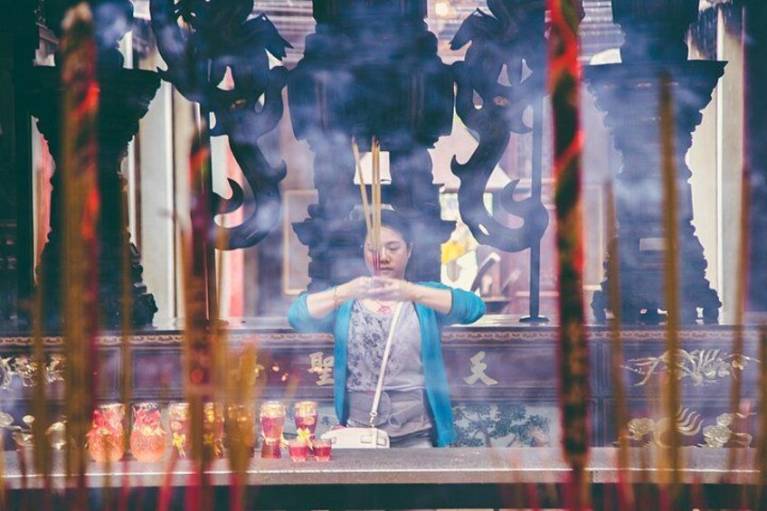 A person in traditional attire performing a ritual with incense sticks in a temple. 2