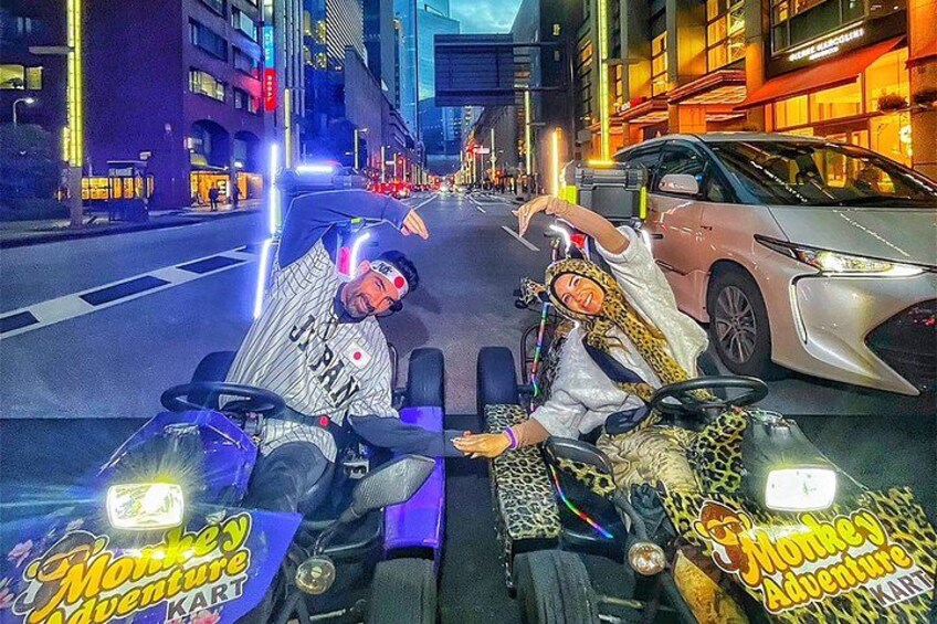 Two people in a vehicle with 'Monkey Adventure' branding, on a city street at night. 4