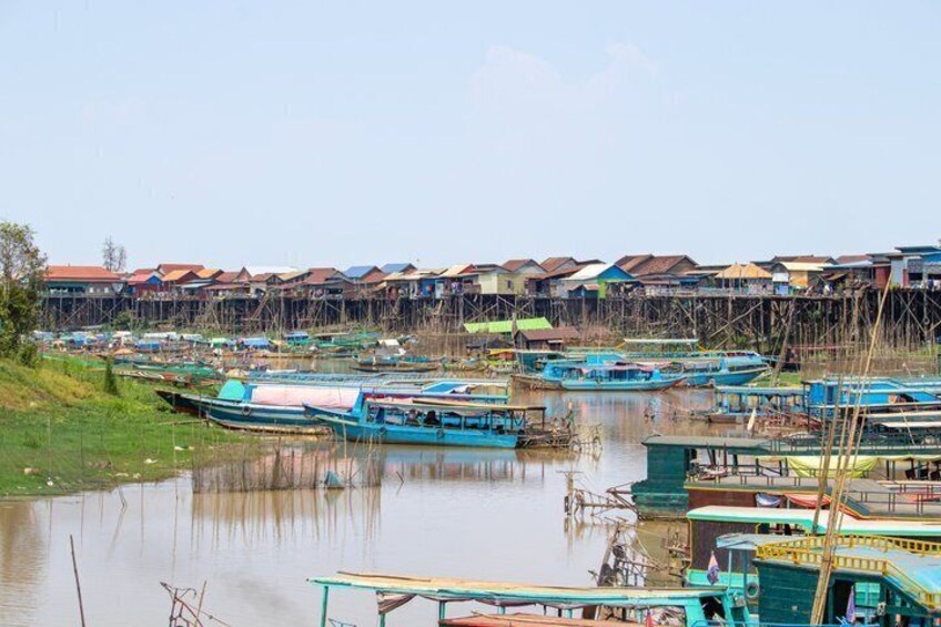 A riverside village with boats docked along the water, wooden houses on stilts, and a calm river. 5