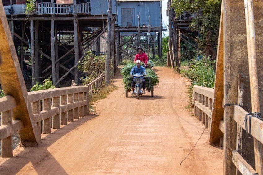 A dirt road flanked by wooden walkways and a person riding a motorcycle. 3
