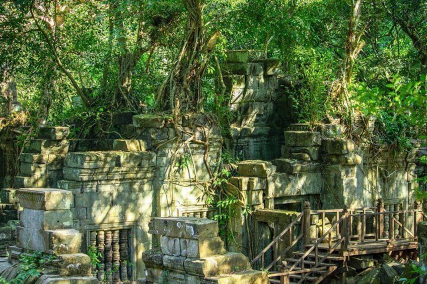 Ancient stone ruins with overgrown vegetation, a wooden bridge, and a stone staircase. 2