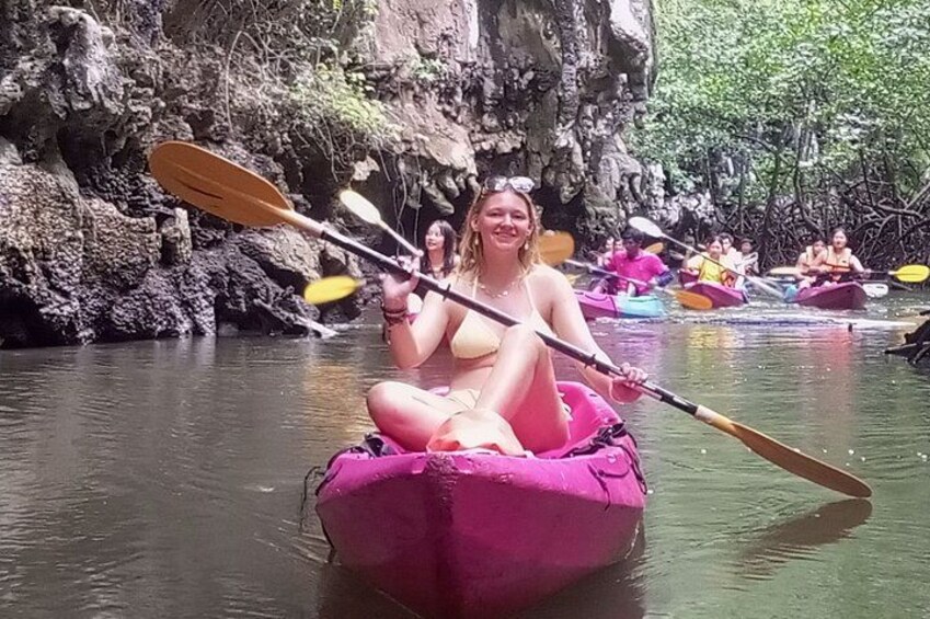 En person i en pink kajak på en flod, med andre personer i baggrunden. 4