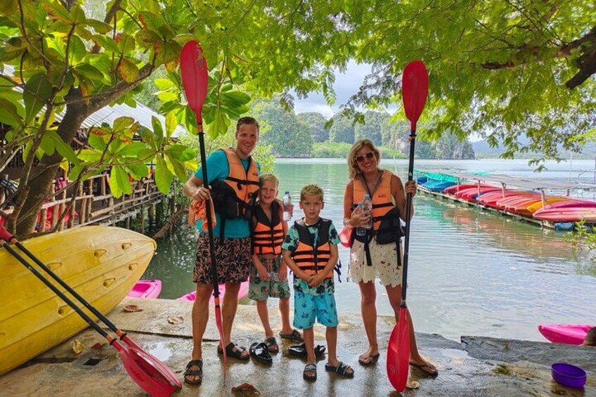 En gruppe mennesker står ved en sø med paddleboards og kajakker. 2