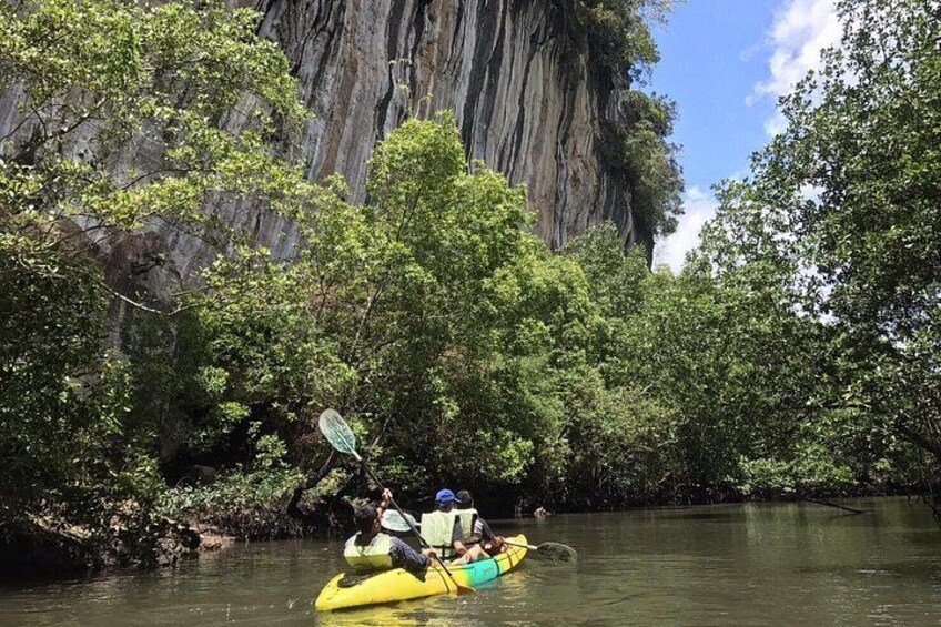 A yellow kayak on a river surrounded by dense greenery and a large rock formation. 1