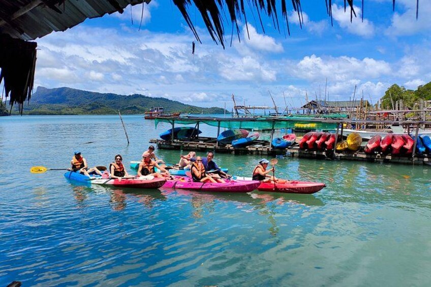 People in kayaks on a calm lake with boats docked in the background. 3