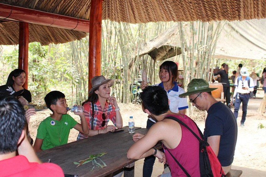 A group of people sitting around a wooden table outdoors, possibly at a campsite or outdoor event. 5
