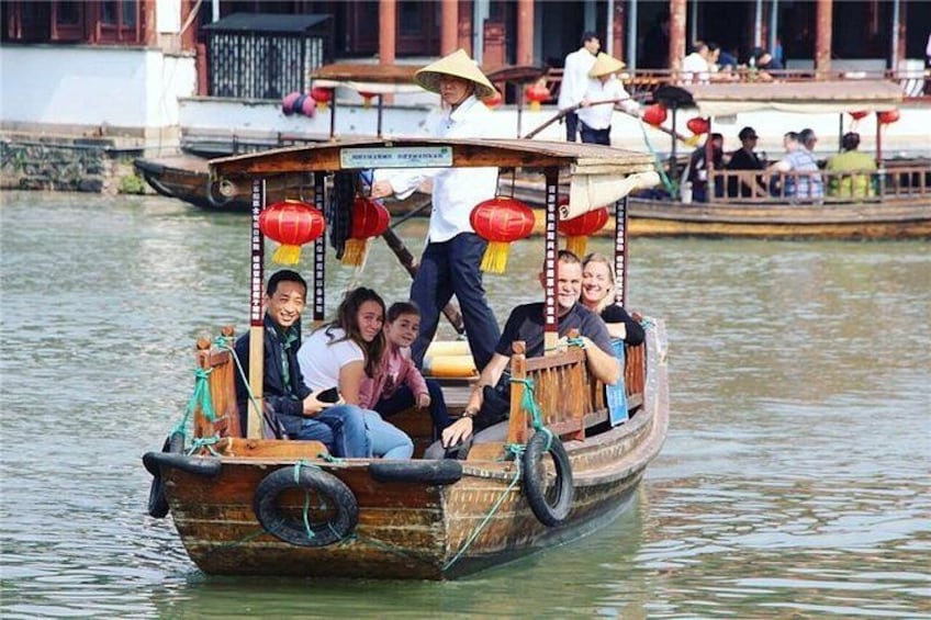 A traditional wooden boat with passengers, a river, and a building in the background. 1