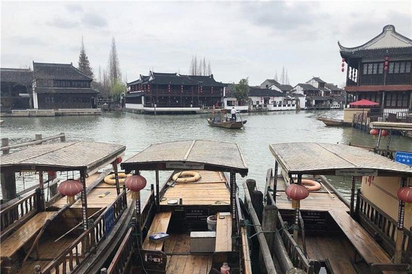 A riverside scene with traditional wooden boats docked, a small boat in the water, and buildings with classic architecture. 5