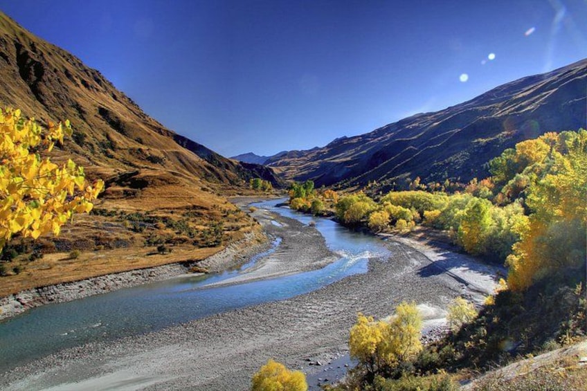 A river winding through a valley with autumn foliage and mountains in the background. 1