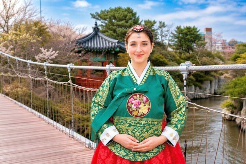 En person i traditionel koreansk hanbok står på en træbro med en pagode i baggrunden. 1