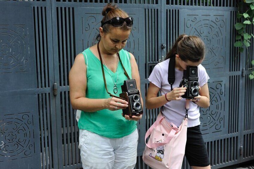 Two individuals with cameras, standing in front of a metal gate. 3