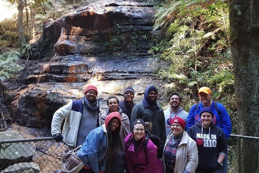 A group of people standing in a rocky outdoor area with a fence and trees in the background. 3