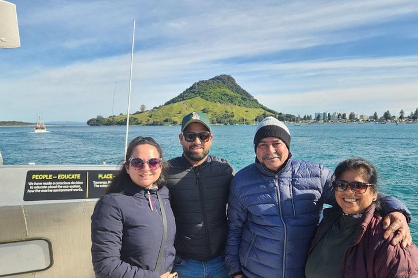 Eine Gruppe von Menschen auf einem Boot, mit einem Schild, auf dem 'PEOPLE-EDUCATE PLACE' steht, und einem grünen Hügel im Hintergrund. 5