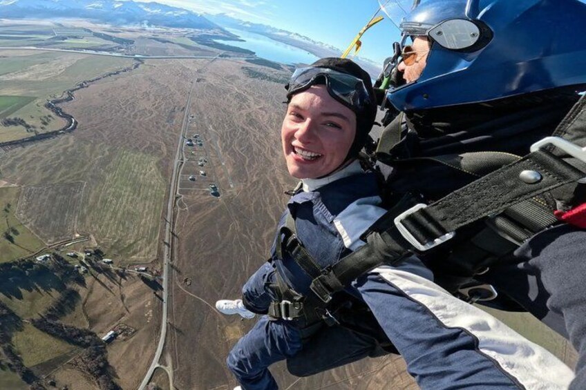 A person skydiving with a parachute, wearing a helmet and harness, with a landscape below. 3