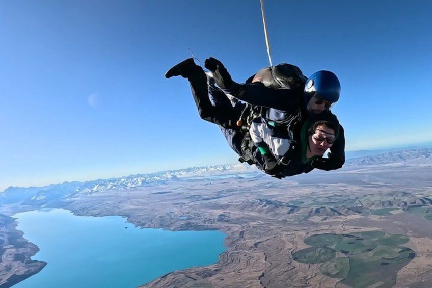 Two individuals skydiving with a mountainous landscape and a body of water below. 4