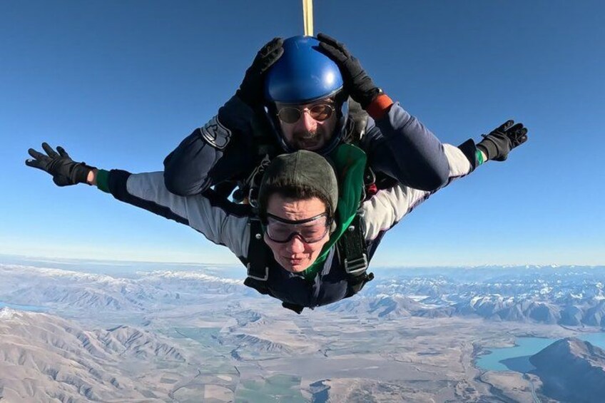 Two skydivers in freefall with a mountainous landscape below. 1