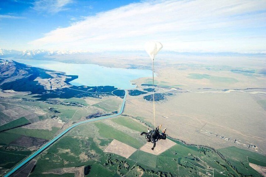 A person skydiving with a parachute over a landscape with fields and a body of water. 5