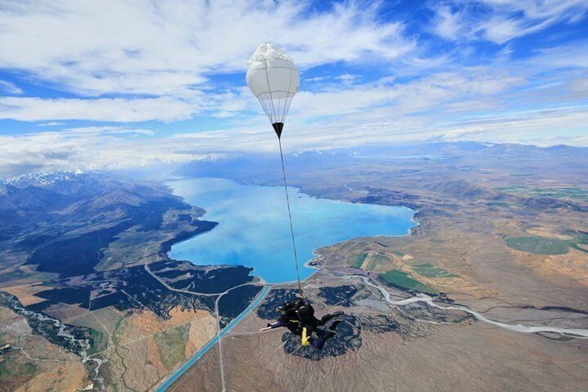 A parachute descending towards a lake surrounded by mountains and fields. 2