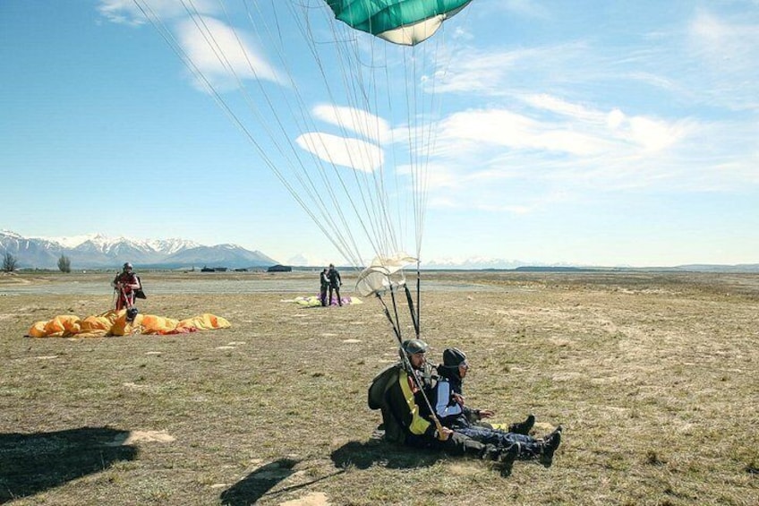 A person preparing to parachute in a grassy field with mountains in the background. 3