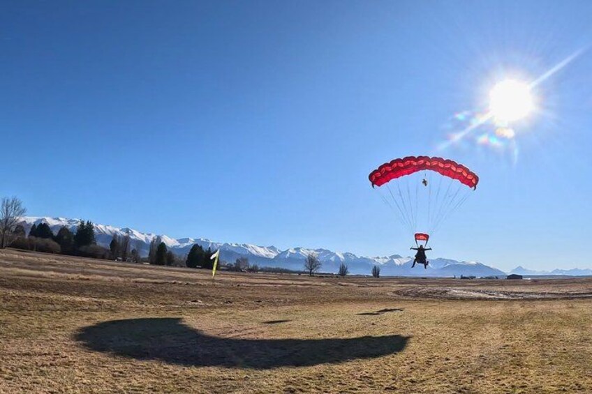 A person paragliding over a grassy field with mountains in the background. 4
