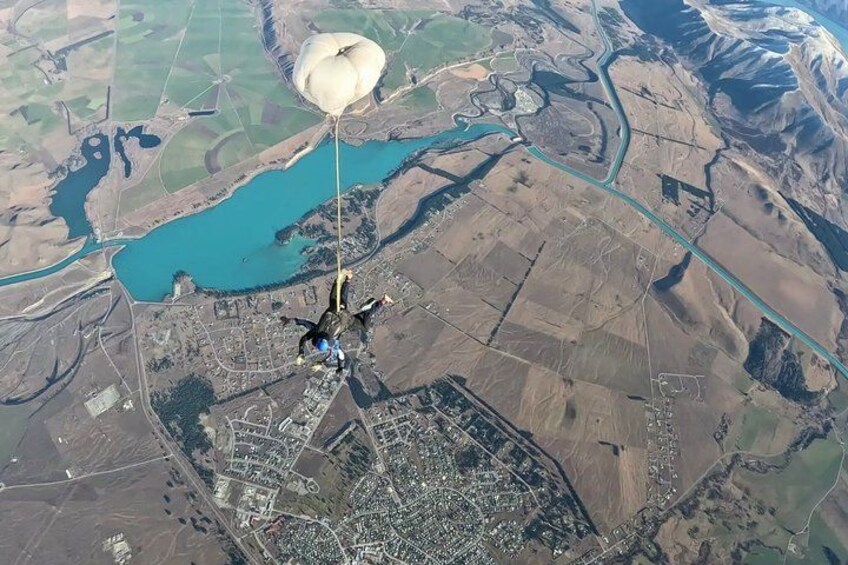 A person skydiving with a parachute over a landscape with a river and fields. 3