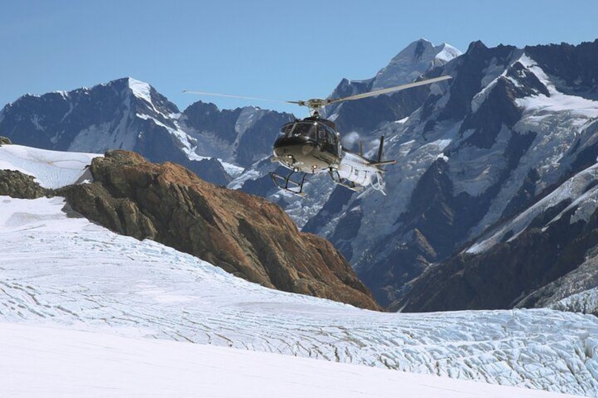 A helicopter flying over a snowy mountain landscape with a rocky outcrop in the foreground. 2