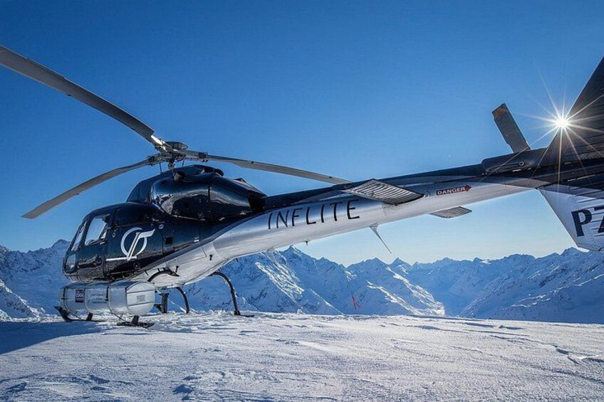A helicopter with 'INFLITE' written on its side, parked on a snowy mountain with a clear blue sky in the background. 2
