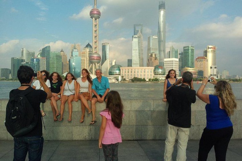 A group of people sitting on a ledge overlooking a city skyline with prominent skyscrapers and a tower. 5