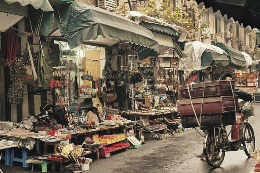 Een levendige openbare markt met diverse kraampjes die waren verkopen, een fiets met een mandje, en een persoon op een motor. 3