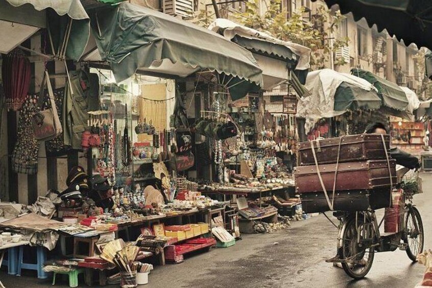 A bustling outdoor market with various stalls selling goods, a bicycle with a load of items, and a person riding a motorcycle. 3
