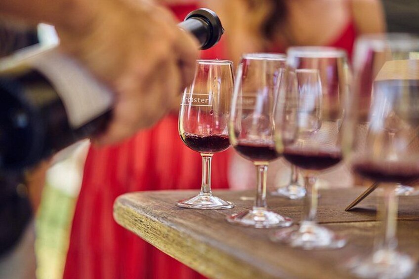 A person pouring wine into a glass on a wooden table. 4